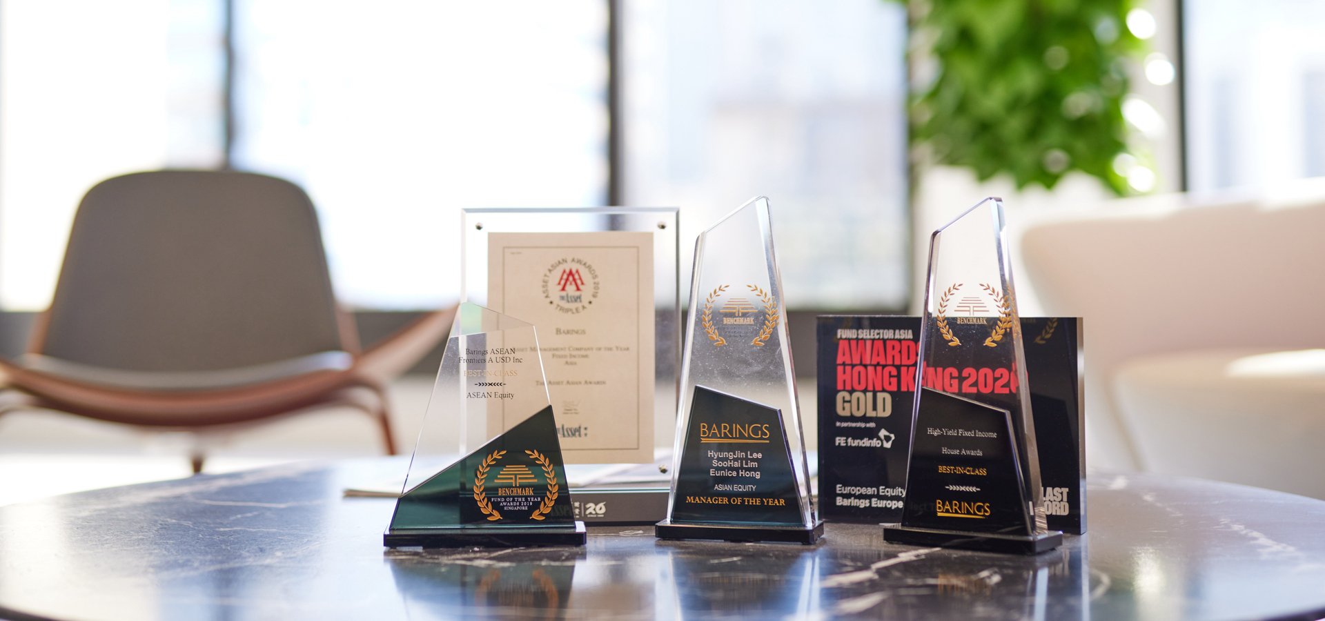A table with several trophies and awards on a low table in front of a skyline view.