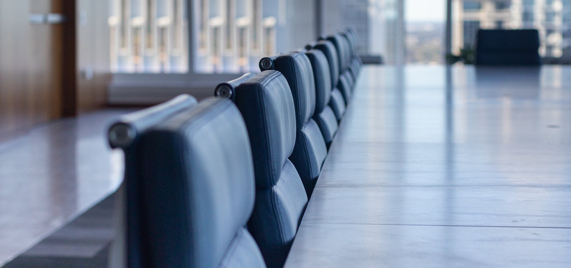A view of blue leather chairs along the side of a marble conference room table with a skyline view in the background.