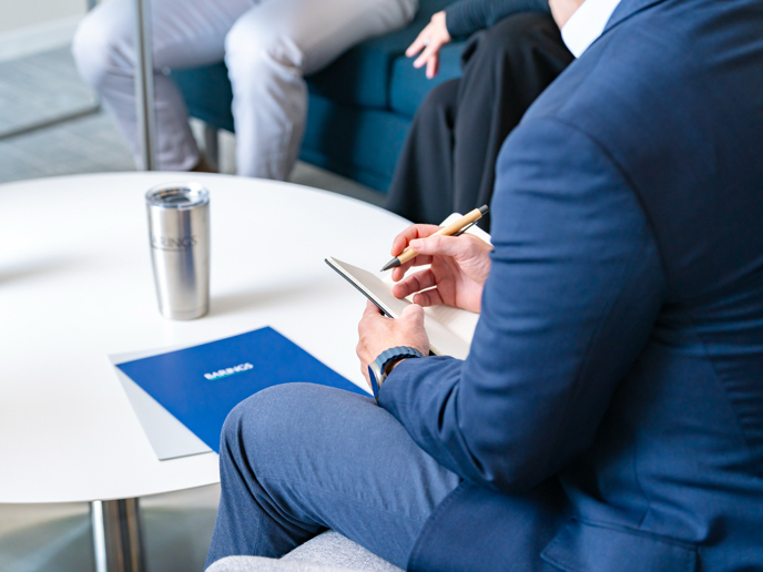 Business person taking notes on a notepad during a client meeting.