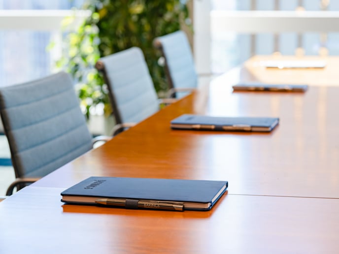 Empty meeting chairs with notepads and pens set up in a meeting space.