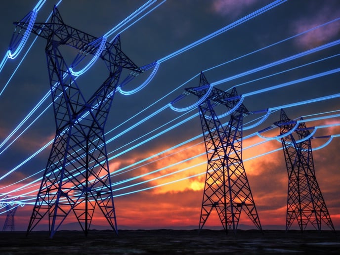 High‑voltage power transmission towers with glowing lines representing electricity flow at sunset.