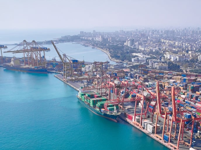 This image shows an aerial view of the Port of Mersin in Turkey. The scene captures a bustling industrial terminal filled with colorful shipping containers and large gantry cranes.
