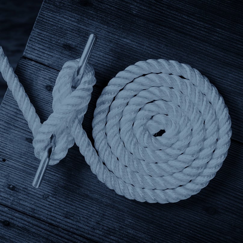 This image shows a white three-strand twisted nylon marine rope tied to a metal cleat on a wooden dock.