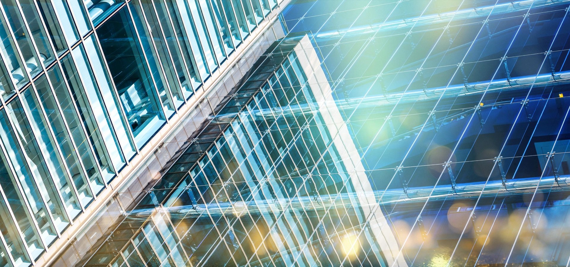 A close-up view of a glass facade of a modern skyscraper. The reflective glass panels create a complex pattern of lines and reflections.