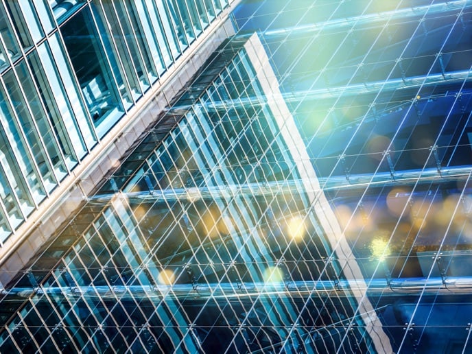 A close-up view of a glass facade of a modern skyscraper. The reflective glass panels create a complex pattern of lines and reflections.