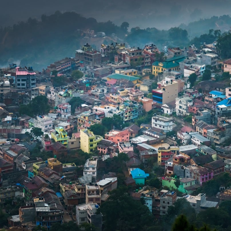 A dense urban hillside in an emerging market, with brightly colored homes stacked closely together amid greenery.