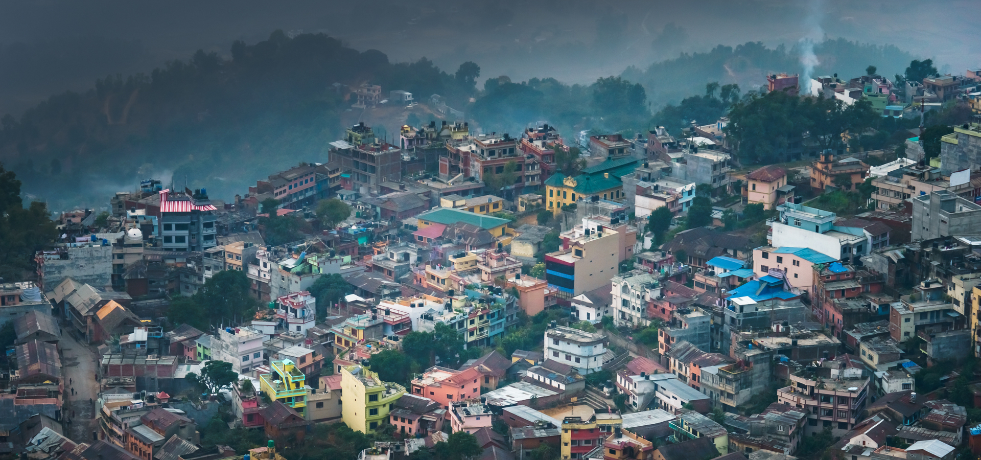 A dense urban hillside in an emerging market, with brightly colored homes stacked closely together amid greenery.