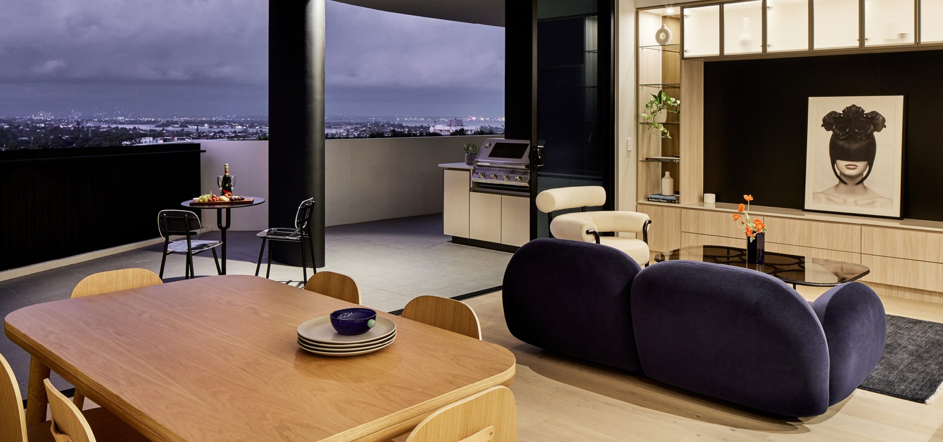 A living room with a table and a couch connected to an open air balcony. 