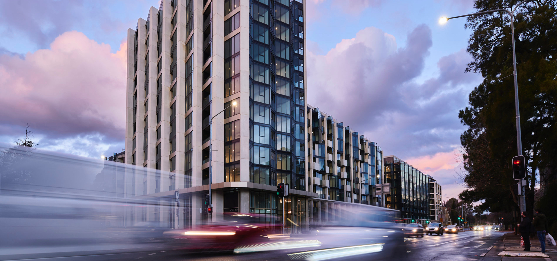 Long shot of a residential building with cars driving in front of it.