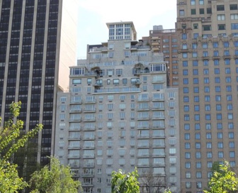 A tall, grey, brick residential building in between two buildings in a city. 