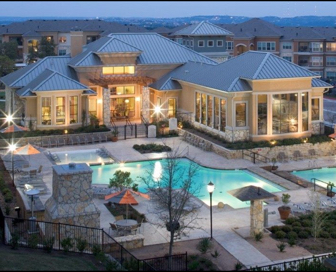 A white, plaster and stone residential clubhouse at dusk with a blue pool in front of it.  