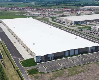 Aerial view of a large white logistics/industrial building with an empty parking lot in front of it. 