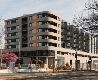 A small brown and orange residential building with a curved corner and construction in front of it. 